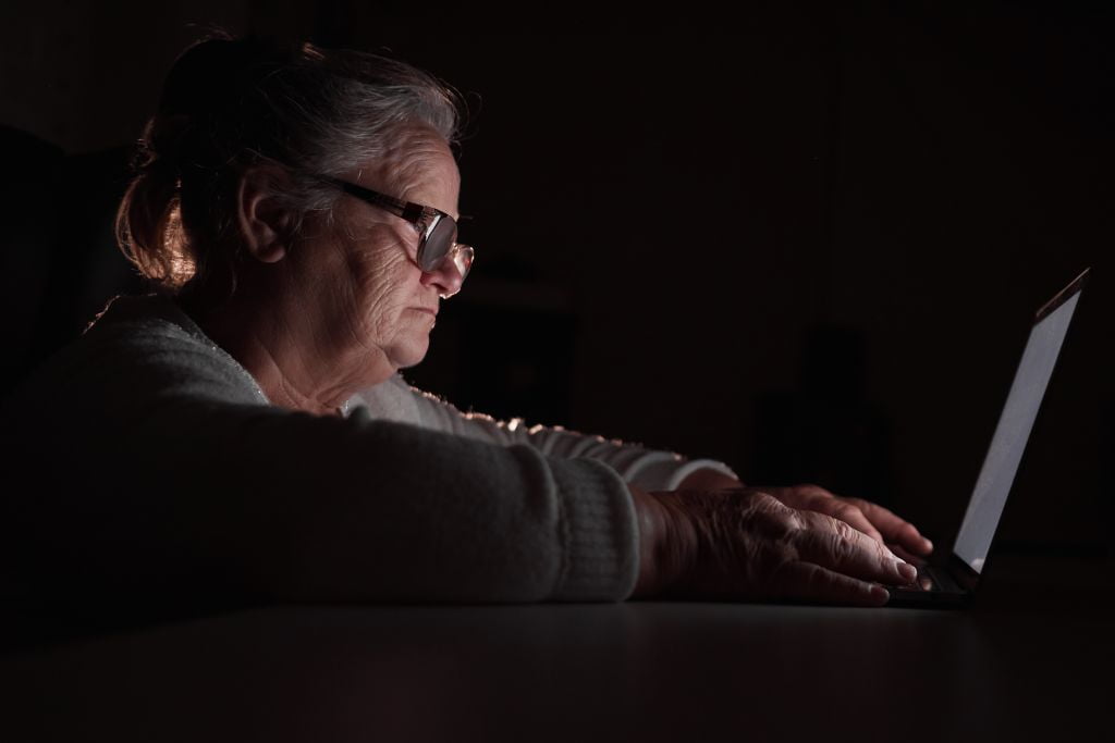 Old overweight woman in darkness using laptop